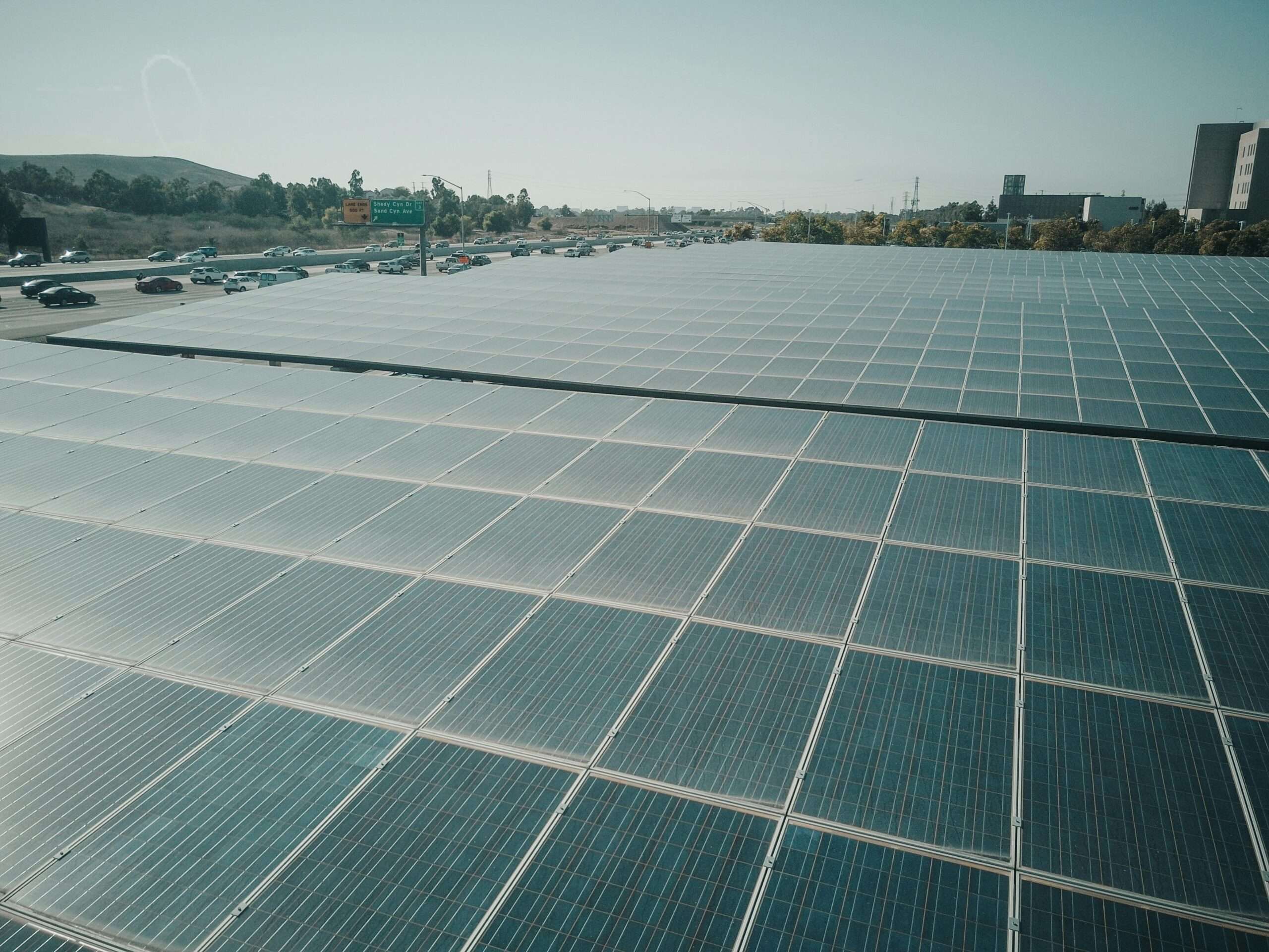 Rows of solar panels near a highway capture renewable energy under a clear sky.